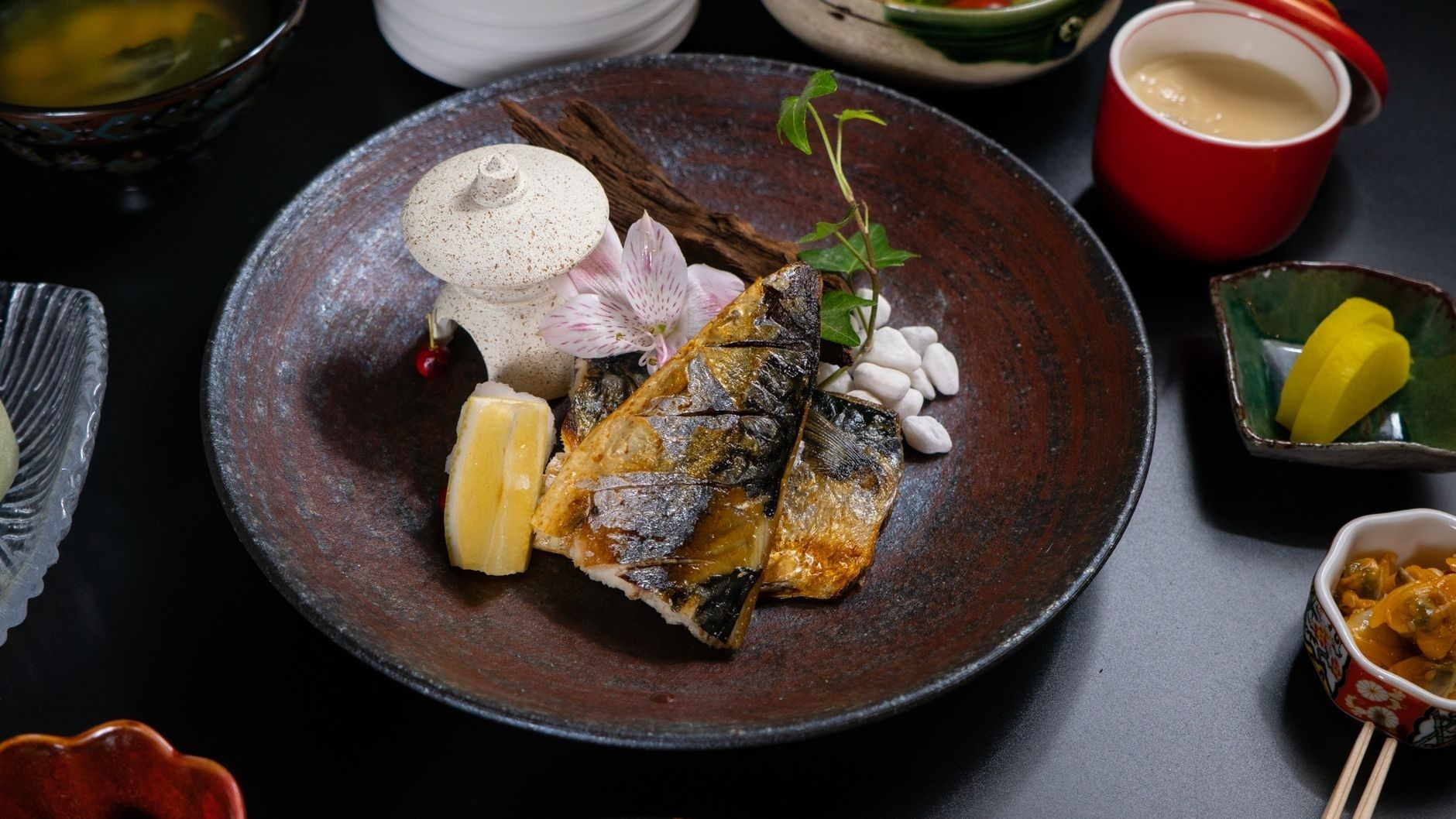 Kaiseki-presentatie met gegrilde vis op een donkere keramische schaal