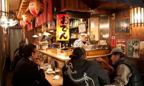 Bezoekers ontspannen aan de bar van een sfeervolle Japanse izakaya